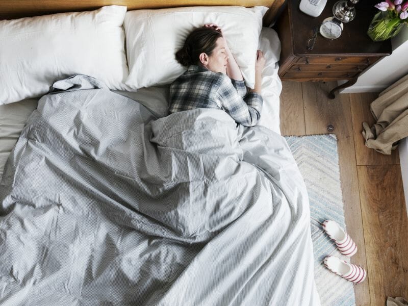 Woman peacefully sleeping in a cozy bed, surrounded by a calm bedroom environment, representing healthy sleep habits and bedtime routines.