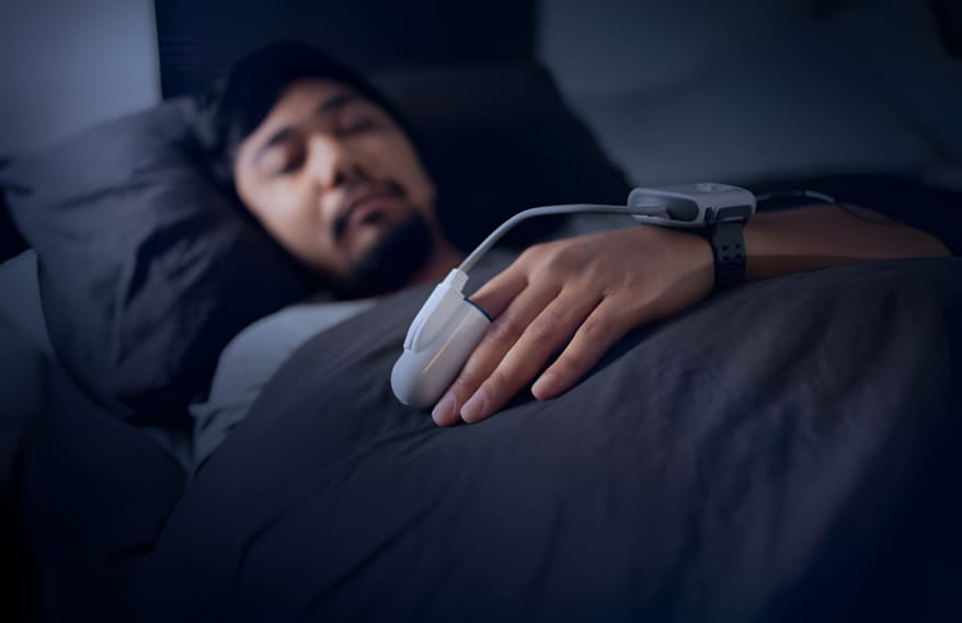 A man sleeping while wearing a sleep apnea test device on his hand and wrist