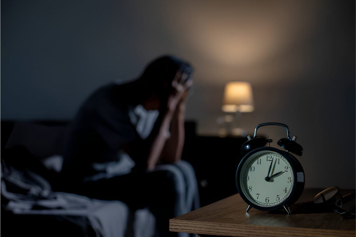 A man sitting on bed in the dark with his head in his hands, struggling with insomnia