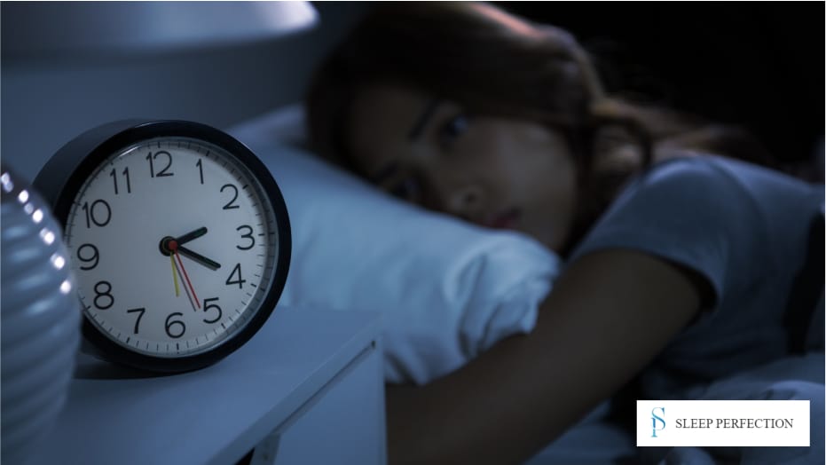 Woman lying in bed at night, staring at the clock on her nightstand, unable to sleep