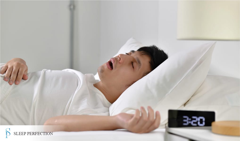 A man sleeps on his back with his mouth open, possibly snoring, with a digital clock showing 3:20 AM