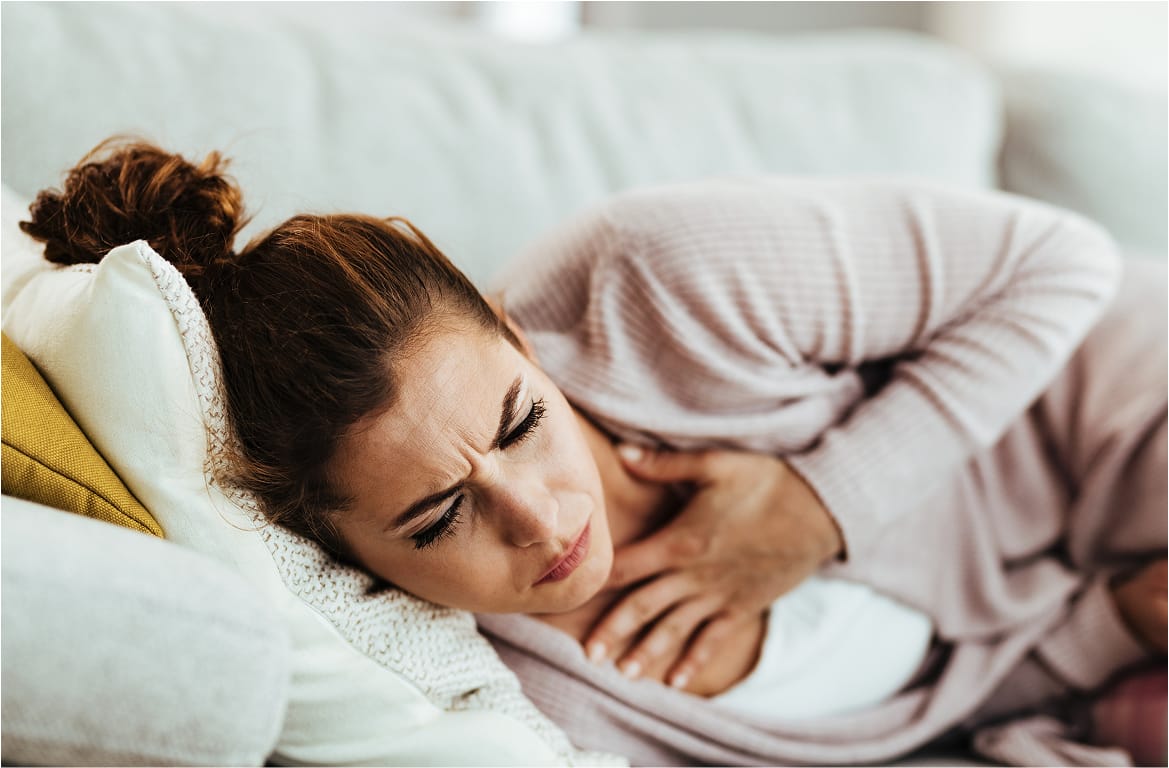A woman lies on a couch holding her chest in discomfort