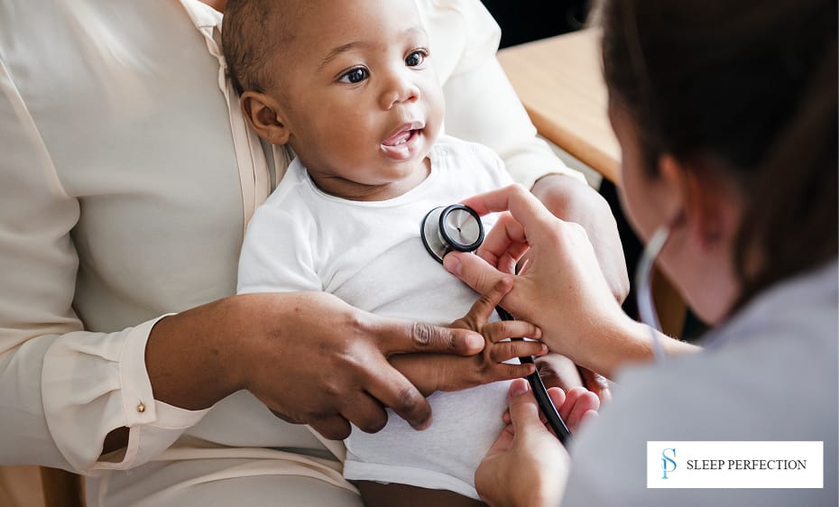 A pediatrician uses a stethoscope to listen to a smiling baby's chest while sitting in the mother's lap