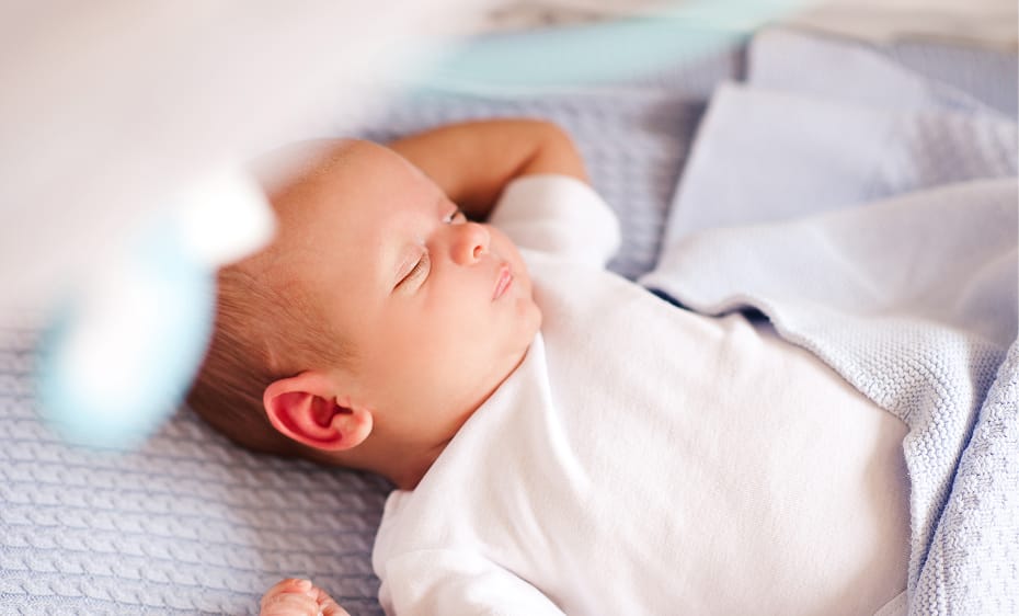 A baby sleeping while snoring on a soft blue blanket while lying on its back with one arm raised